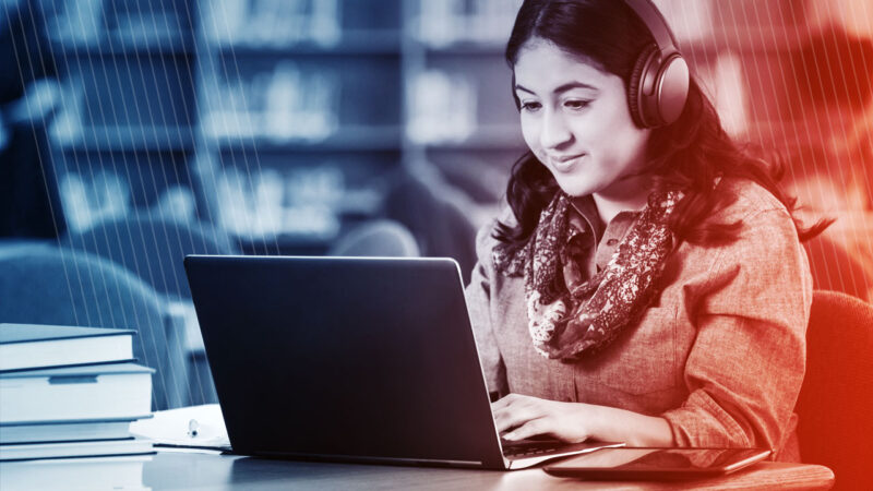 Photo of female college student using laptop in library